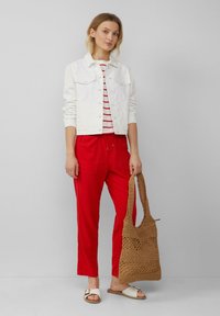 Biała dżinsowa kurtka, czerwone spodnie z wszytymi sznurkami, pasiaste top i pleciona jasnobrązowa torba. Stylizacja zawiera płaskie białe sandały i luźny krój.