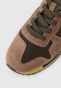 Close-up of brown and black sneaker toe with textured suede and thick laces on a light background.