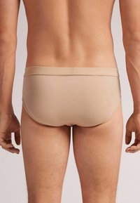 Beige Baumwollslips mit glatter Textur und niedrigem Bund, ausgestattet mit einem schlichten elastischen Taillenbund und einer engen Passform.