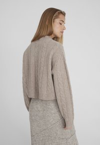 Hellbeiger, kurz geschnittener Pullover mit Zopfmuster, geripptem Saum und Ärmeln, kombiniert mit einem strukturierten, hellbeigen Rock.