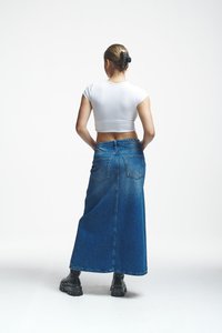 Középkék farmer maxi szoknya, magas derékkal, hátsó zsebekkel és enyhén bővülő fazonnal. Feszes, fehér crop top-pal és fekete csizmával párosítva.