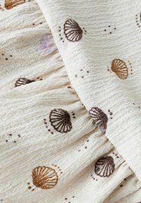 Textured cream fabric featuring embroidered shell patterns in brown and orange, with subtle dots, creating a layered, soft appearance.