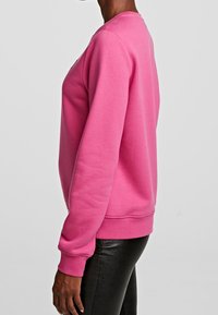 Sudadera rosa con cuello redondo, puños y dobladillo acanalados. Textura suave y corte ligeramente holgado. Combinada con leggins negros.