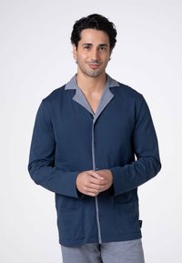 Giacca in cotone blu navy con colletto grigio, chiusura con bottoni e due tasche frontali. Tessuto morbido, vestibilità comoda, adatta a un abbigliamento casual.