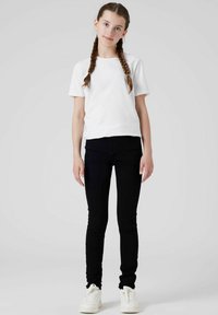 Fehér rövidujjú póló fekete skinny farmernadrággal és fehér sportcipővel párosítva. Egyszerű dizájn, laza szabás és egyszínű árnyalatok.