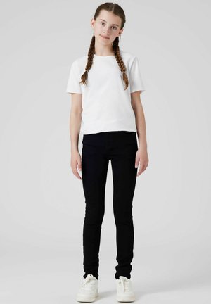 Camiseta blanca de manga corta combinada con jeans skinny negros y sneakers blancos. Diseño simple, corte casual y colores sólidos.
