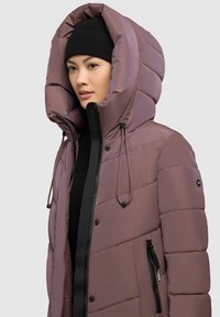 Polstret jakke i dæmpet mauve med en stor hætte, lynlåse og snører detaljer. Har en glat tekstur og sorte accenter.