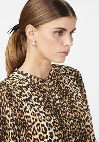 Blusa con stampa leopardata, collo a cappotto, texture plissettata e dettagli con bottoni, mostrata su uno sfondo neutro.