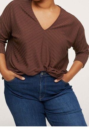Bruine, geribbelde V-hals top met driekwart mouwen, geknoopt in de taille, gecombineerd met blauwe spijkerbroeken met knoopsluiting en zijzakken.