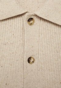 Beige stickad cardigan med ribbad textur, spetsig krage och tre runda, ljusbruna knappar fram.