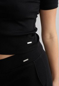 Schwarzes, geripptes Oberteil mit kurzen Ärmeln, kombiniert mit passenden schwarzen Hosen. Silberne Hardware-Elemente am Saum und am Bund.