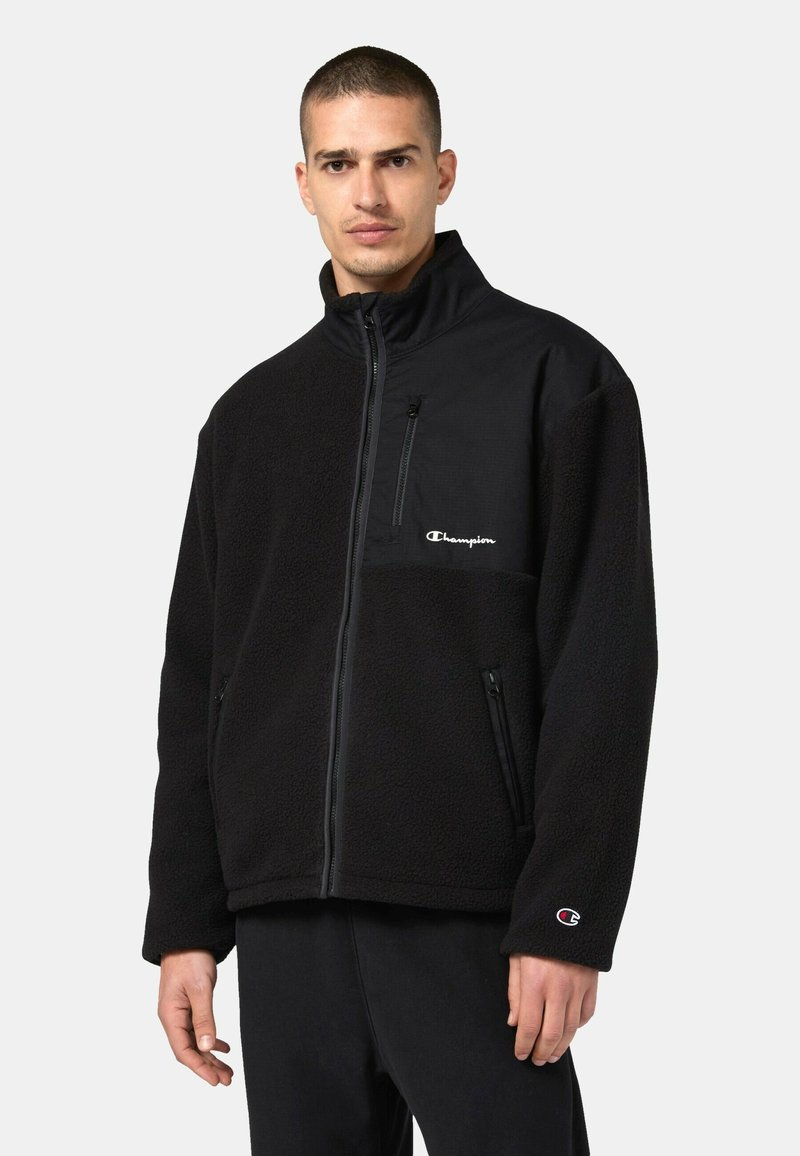 Schwarze Fleecejacke mit hohem Kragen, Reißverschlusstaschen und Champion-Logo. Hat eine weiche Textur und kontrastierende Stoffpaneele.