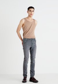 Vaaleanruskea hihaton paita yhdistettynä harmaisiin farkkuihin. Slim fit -malli, jossa on hillitty kuluminen. Tummatnahkakengät viimeistelevät asukokonaisuuden. Yksinkertainen, siisti muotoilu.