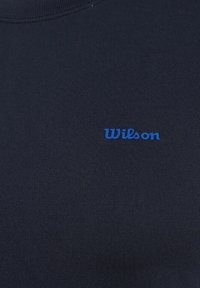 Sudadera azul marino con cuello redondo, fabricada en un tejido suave. Cuenta con un pequeño logo azul de "Wilson" en el frente. Textura suave en general.