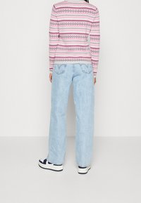 Jeans larges bleu clair associés à un pull à motifs rose et gris. L'ensemble comprend des baskets blanches avec des accents bleu marine.