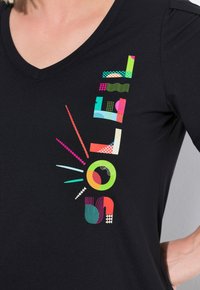 Zwarte T-shirt met een v-hals, voorzien van kleurrijke abstracte grafische patronen in verschillende vormen, waaronder cirkels, lijnen en geometrische ontwerpen.