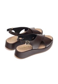 Sandales en cuir marron avec des sangles croisées, une semelle plateforme et une fermeture à boucle. Semelle intérieure douce avec une marque dorée sur la semelle.