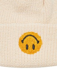 Strikket beanie i lys beige med en tekstureret overflade. Har et rundt, gult smilende ansigt broderet på forsiden med sorte accenter.