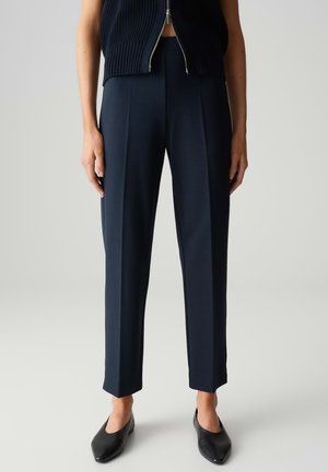 Pantaloni sartoriali blu navale realizzati in tessuto morbido, caratterizzati da un design a gamba dritta con pieghe frontali e caviglie orlate, abbinati a ballerine nere.