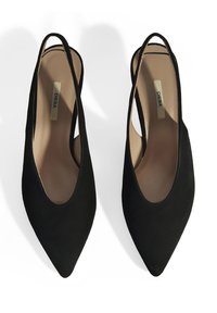 Chaussures slingback en daim noir avec bout pointu, présentant des côtés ouverts et une doublure intérieure lisse. Étiquette de marque subtilement visible à l'intérieur.
