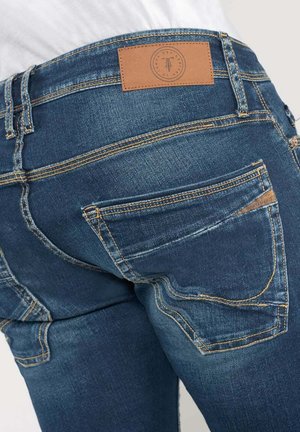 Denimjeans i mellemblå farve, fem-lomme design, kontrastfyldt gul syning og en brun læderlap på taljen.