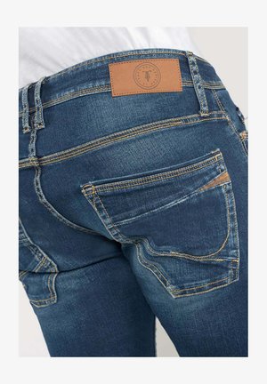 Spijkerbroek in een medium blauwe kleur, vijf-pocketdesign, contrasterende gele stiksels en een bruine leren patch op de tailleband.