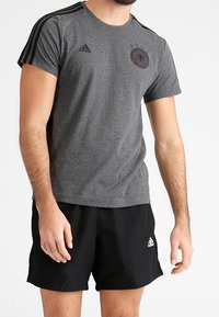 Harmaa urheilu T-paita, jossa on mustat raidat hartioilla, brändin logo ja tunnus. Yhdistetty mustiin shortseihin, joissa on valkoinen logo.