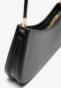 Black leather handbag with a slim, structured design. Features gold hardware and a zip closure, showcasing smooth texture and clean lines.