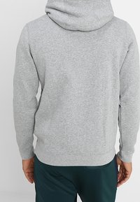 Harmaa huppari, joka on valmistettu pehmeästä puuvillasekoitteesta. Siinä on suuri säädettävä huppu, pitkät hihat ja istuva vyötärökaitale, yksinkertaisella muotoilulla.