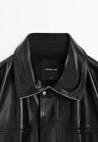 Shiny black leather jacket with a wide collar, silver zipper detail, and a visible Massimo Dutti label inside the neckline.