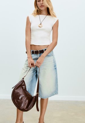 Weißes enges Cropped-Top, hellblaue, hochtaillierte Denim-Culottes, braune Lederhandtasche und eine goldene Anhängerhalskette. Glatte und entspannte Texturen.