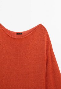 Gestrickter Pullover in verbranntem Orange, mit weitem Boot-Ausschnitt und langen Ärmeln. Die Struktur ist lockeres Gestrick, das leichte Lücken im Stoff offenbart.