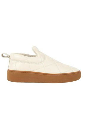 Chaussure slip-on couleur crème avec dessus matelassé et semelle épaisse en caoutchouc marron, avec une languette à l’arrière et un design bas au niveau de la cheville.