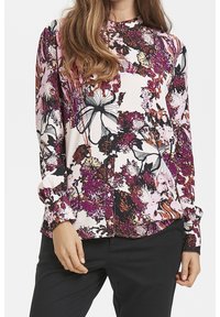 Camisa de botones con estampado floral que presenta un patrón en tonos rosa, negro y púrpura sobre un fondo claro, con mangas largas y cuello redondo.