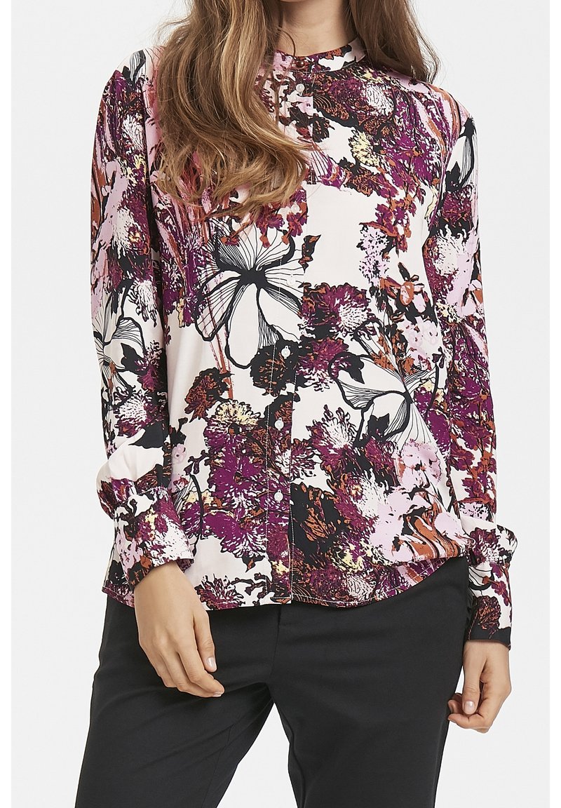 Camisa de botones con estampado floral que presenta un patrón en tonos rosa, negro y púrpura sobre un fondo claro, con mangas largas y cuello redondo.