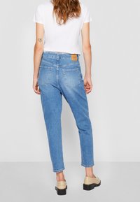 Light blue denim high-waisted jeans with a tapered leg, featuring back pockets and a brown leather logo patch at the waistband.