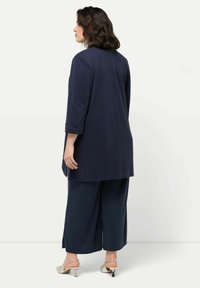 Mörkblå tunika med trekvartslånga ärmar, som har en avslappnad passform som sträcker sig under höfterna. Tillsammans med vida mörkblå byxor och metalliska klackar.