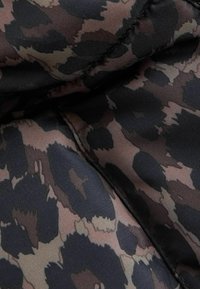 Tekstura u leopard uzorku s nijansama smeđe, crne i krem boje, glatke površine i suptilnog sjaja, sa crnim šavom.
