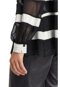 Blouse rayée noir et blanc avec des manches transparentes, présentant des poignets froncés et un détail de bouton au poignet. Texture lisse, légère et aérienne.