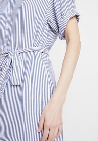 Blå och vit randig klänning med korta ärmar, knappstängning framtill och knytning i midjan. Mjukt tyg med en avslappnad passform och ledig design.