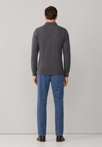 Polo à manches longues gris foncé avec col, associé à un pantalon bleu clair. La tenue comprend des chaussures en cuir marron foncé. Design simple et ajusté.