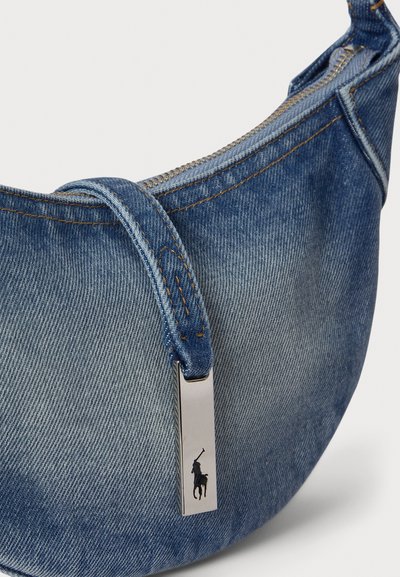 Ívelt alakú farmer anyagú táska világoskék színben, kontrasztos varrással, cipzáras záródással, és egy fém tábla ló logóval.