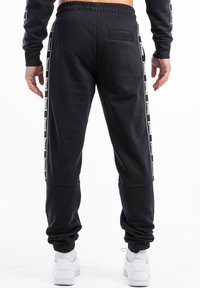 Pantalones de chándal negros con detalles de franjas laterales, cinturilla elástica y tobillos ajustados. Fabricados con una tela suave y un ajuste relajado.