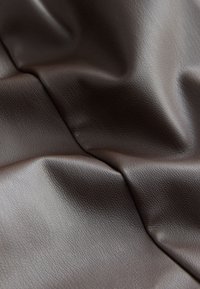 Brun tekstureret kunstlæderstof med rynker og folder, der viser en subtil mønster og en glat overflade samlet set.