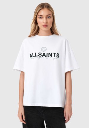 Mlada žena s ravnom plavom kosom nosi bijelu oversized majicu s natpisom "ALLSAINTS" i malim grafikonom globusa.