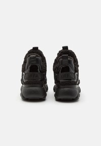 Zwarte sportieve sneakers met gepatenteerd leer en pluizige textielaccenten, voorzien van een trekband en reliëfbranding op de hiel.