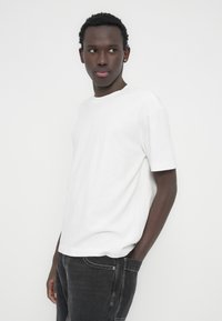 Λευκό βαμβακερό T-shirt με στρογγυλή λαιμόκοψη και κοντά μανίκια, συνδυασμένο με παντελόνι ντένιμ σε σκούρο γκρι χρώμα. Ομαλή υφή και άνετη εφαρμογή.