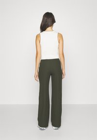 Ribbade olivgröna vida byxor i kombination med en vit ärmlös topp; mjukt tyg med subtila sömdetaljer runt halsringningen.