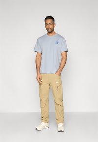 Ανοιχτό μπλε βαμβακερό μπλουζάκι με κοντά μανίκια και λογότυπο, σε συνδυασμό με μπεζ παντελόνι cargo με δύο πλαϊνές τσέπες και ελαστικά τελειώματα. Άσπρα αθλητικά παπούτσια.