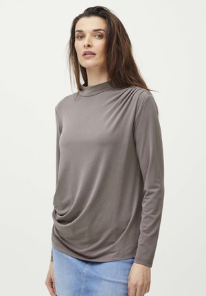 Long-sleeved, gray top with a high neckline, featuring draped fabric and a textured shoulder detail, worn with a denim skirt.
